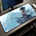 A large desk mat with a detailed anime-style illustration of a female warrior character, shown on a desk next to a keyboard, mouse, and monitor.